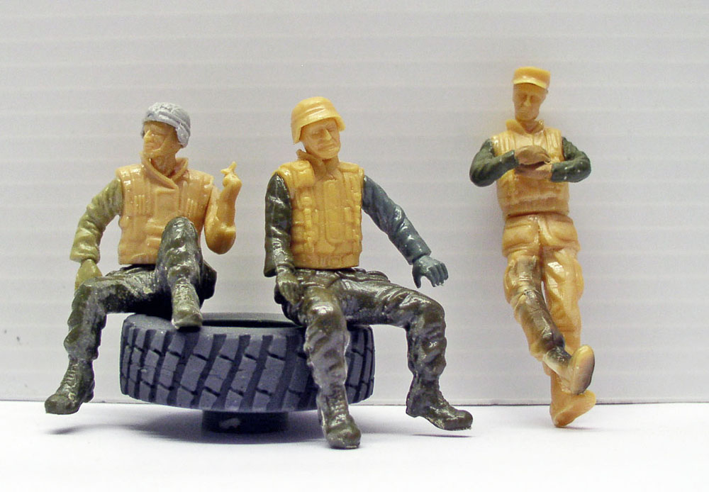 Trois figurines de soldats en gilet pare-balles, deux assis sur un pneu