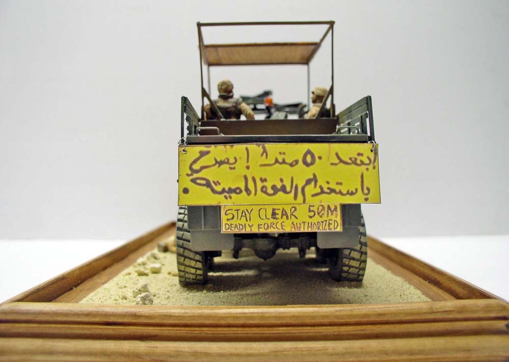 Vue arrière de la maquette M923 Big Foot avec panneau jaune d'avertissement bilingue sur diorama de sable