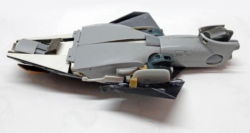 Maquette de vaisseau spatial gris en cours d'assemblage maintenue par du ruban adhésif