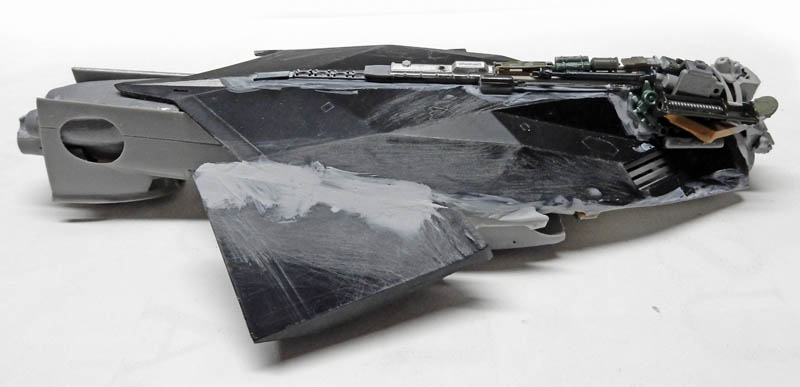 Maquette de vaisseau spatial en construction avec mastic appliqué et détails électroniques sur fuselage gris foncé