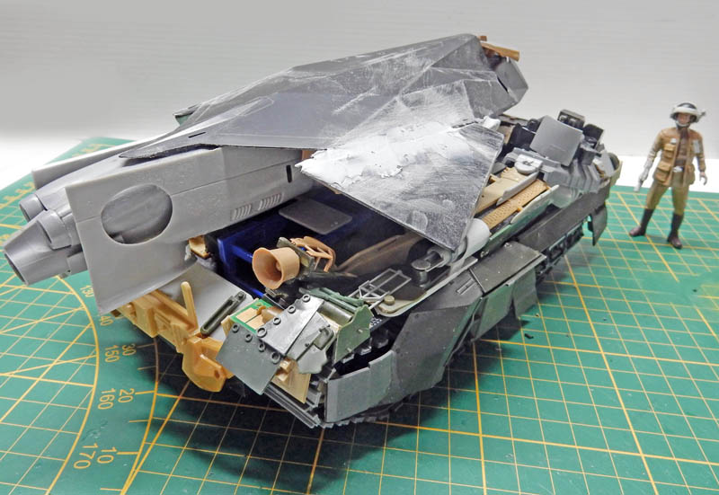 Maquette de véhicule militaire futuriste en construction, intérieur détaillé visible, avec figurine de pilote sur tapis de découpe