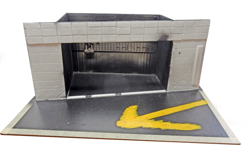Maquette de hangar gris avec ouverture béante et marquages jaunes peints sur le tarmac
