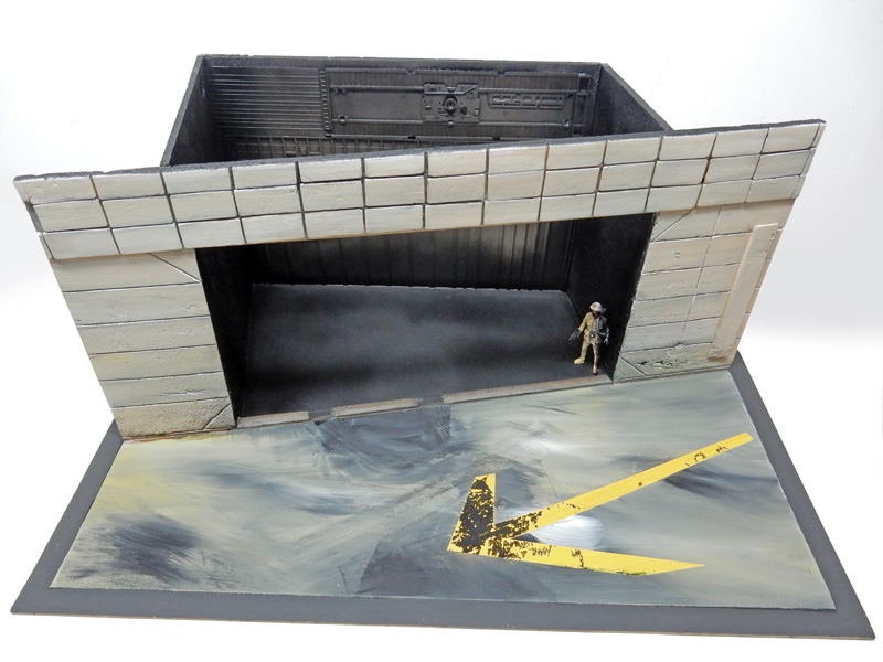 Maquette de hangar industriel en béton avec figurine et flèche jaune au sol