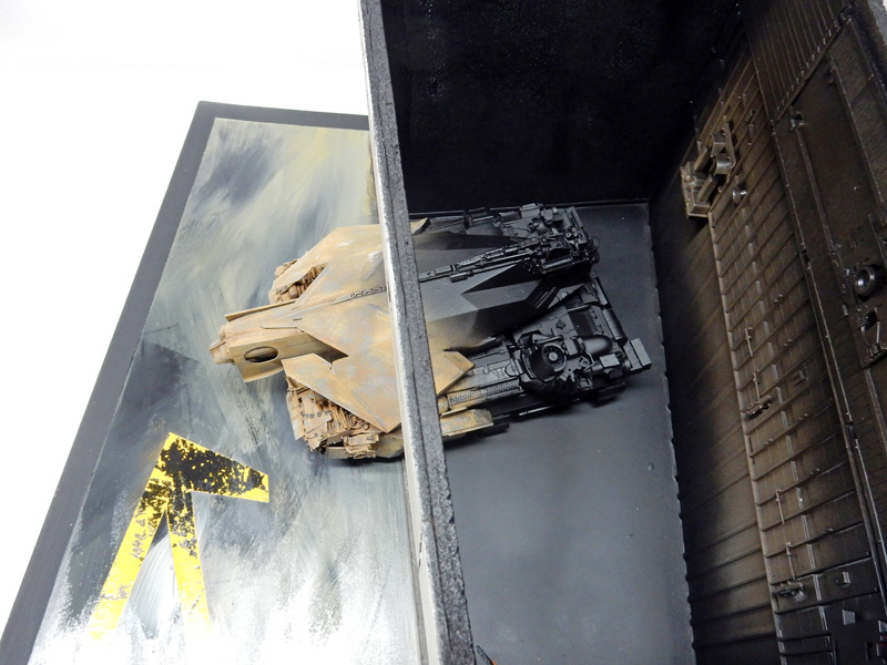 Maquette de véhicule blindé futuriste dans un diorama de hangar industriel avec marquage jaune au sol