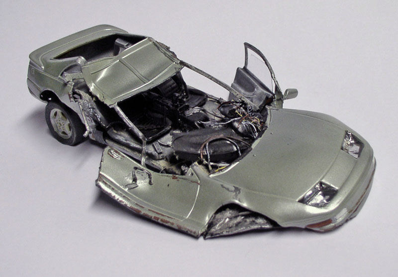 Maquette de voiture de sport argentée accidentée, carrosserie déformée et intérieur détaillé sur fond clair
