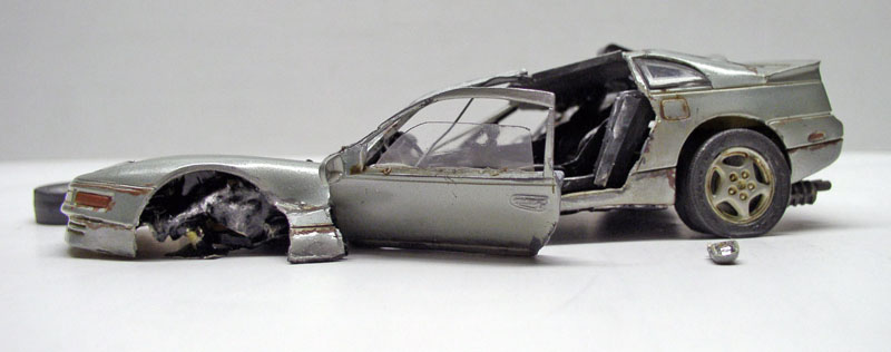 Maquette de voiture de sport argentée endommagée, carrosserie ouverte et avant accidenté sur fond clair