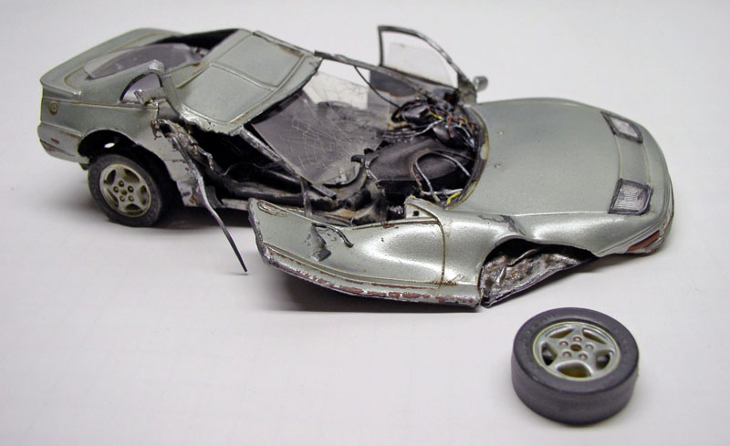 Maquette de voiture de sport argentée accidentée, carrosserie écrasée et une roue détachée posée à côté
