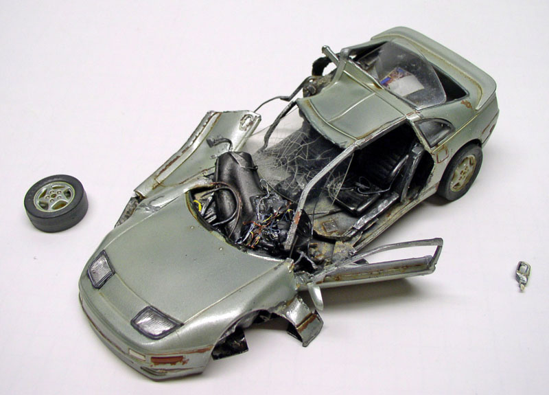 Maquette de voiture de sport grise accidentée, carrosserie déchirée, roue et pièce détachées