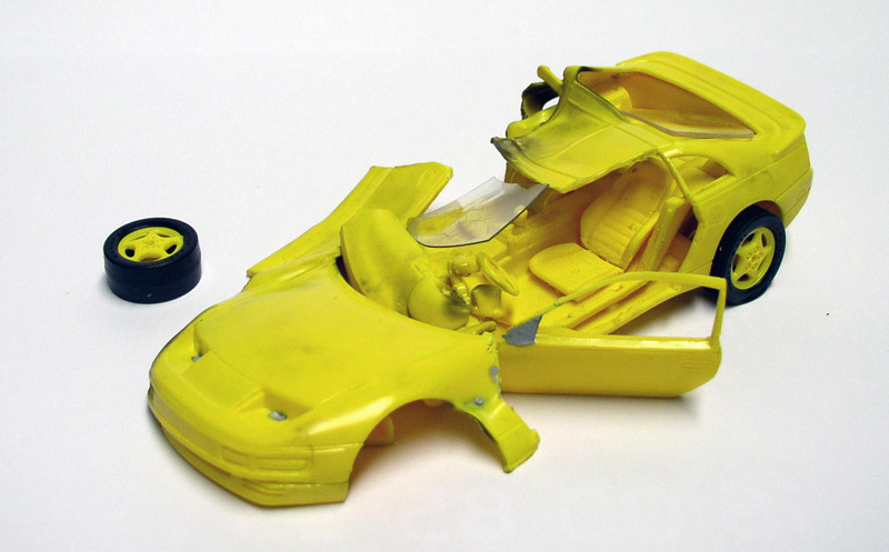Maquette de voiture de sport jaune en cours d'assemblage avec roue détachée