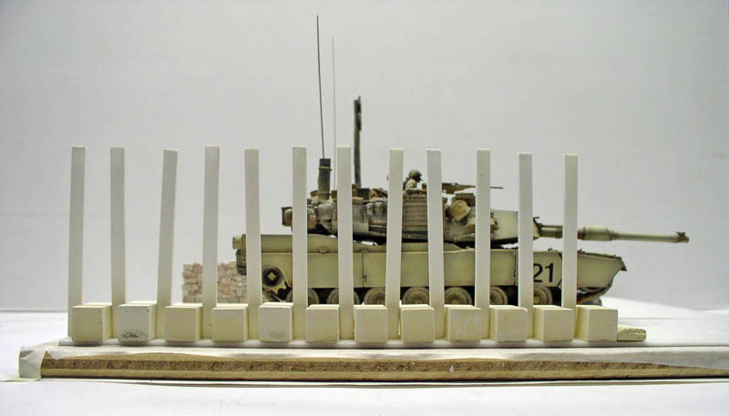 Maquette de char Abrams M1 A1 beige derrière une rangée de poteaux blancs