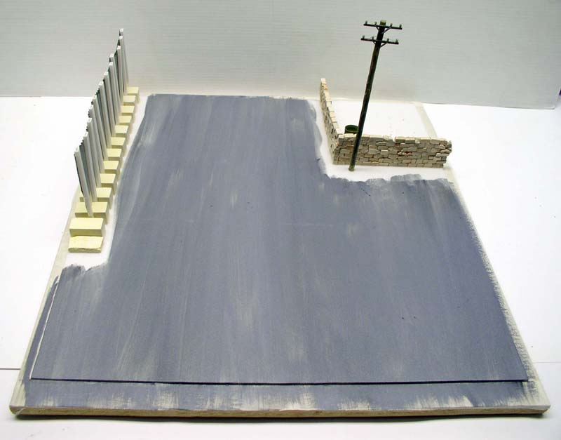 Diorama en construction avec sol peint en gris, mur de briques et poteau électrique