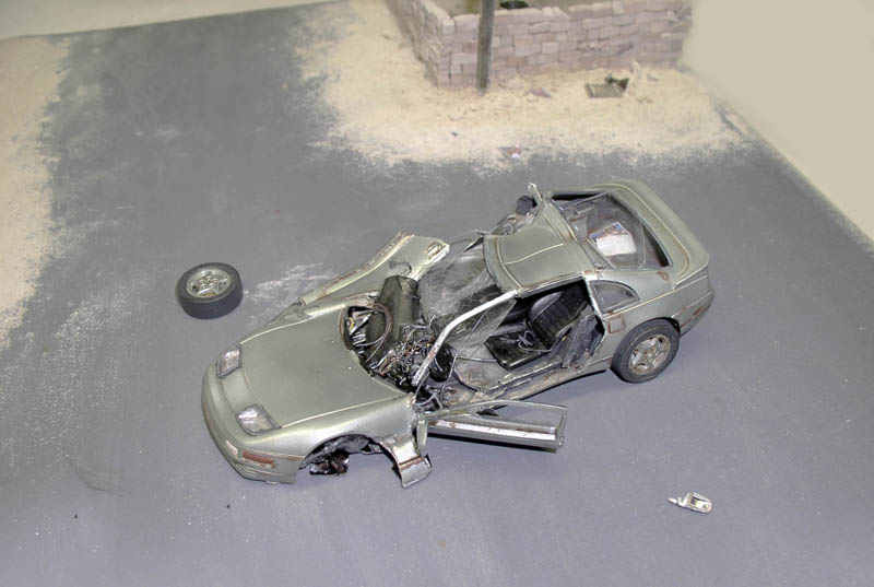Maquette de voiture de sport détruite et écrasée, roue arrachée, sur un diorama urbain