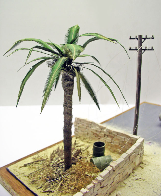Diorama de maquette avec palmier, muret de briques et poteau électrique sur sol sableux