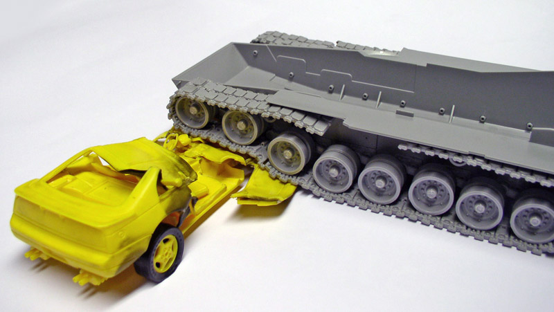 Maquette de char Abrams gris écrasant une voiture jaune broyée sous ses chenilles