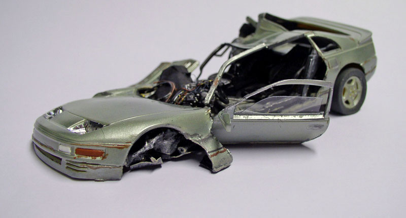 Maquette de voiture de sport grise accidentée, carrosserie déchirée et portière ouverte sur fond clair