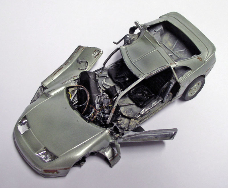 Maquette de voiture de sport accidentée, carrosserie grise éventrée révélant l'habitacle et le moteur détaillés