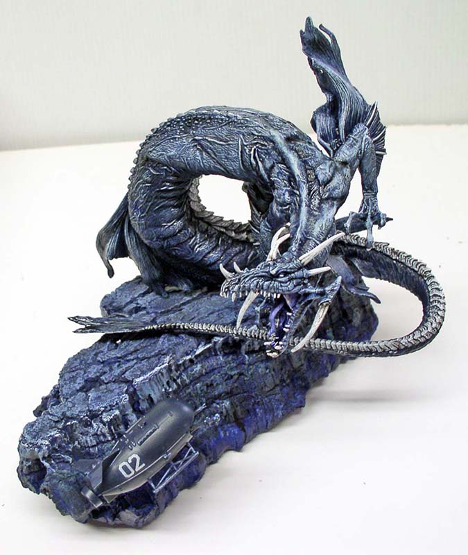 Maquette de dragon marin bleu menaçant un petit sous-marin numéroté 02 sur socle rocheux