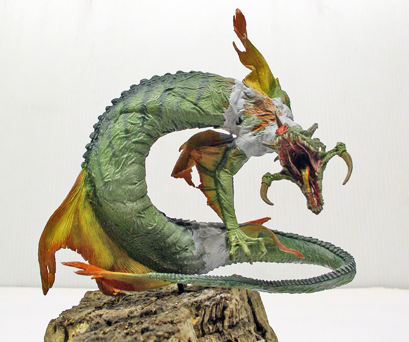 Figurine peinte de créature marine serpentine verte aux nageoires orange, gueule ouverte sur socle