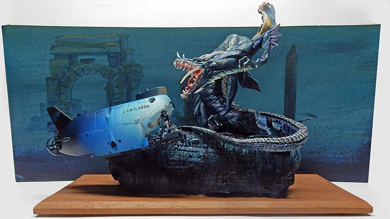 Diorama sous-marin avec sous-marin bleu et créature serpentine géante devant des ruines englouties