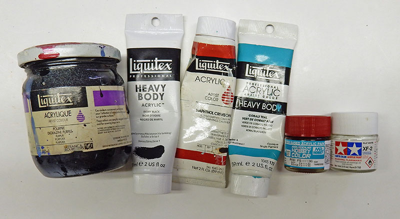 Pots et tubes de peinture acrylique Liquitex et Tamiya pour aérographe alignés sur une table