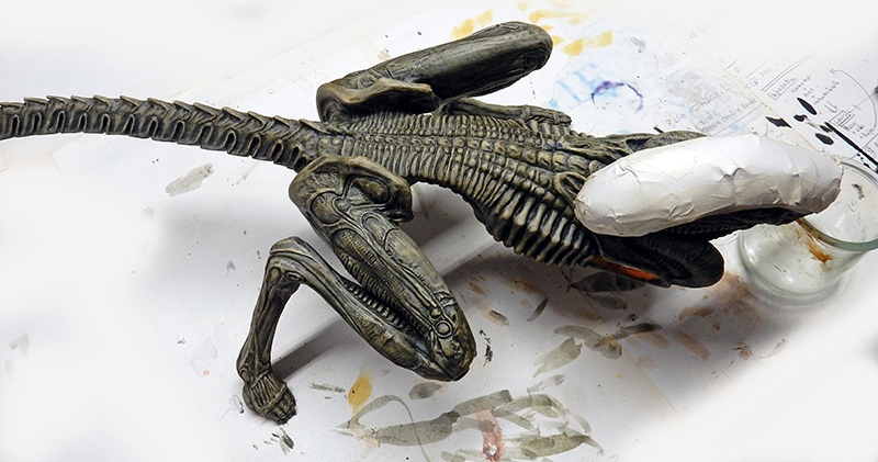 Maquette du xénomorphe d'Alien 3 peinte en gris-vert, posée sur un plan de travail taché