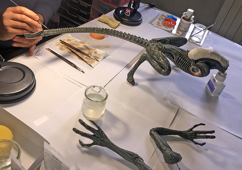 Maquette de l'Alien d'Alien 3 en cours de peinture sur un plan de travail avec pinceaux