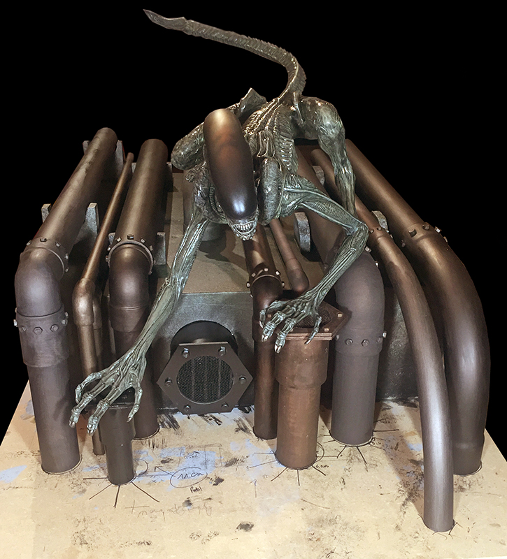 Maquette du xénomorphe d'Alien 3 accroupi sur une structure industrielle de tuyaux cuivrés