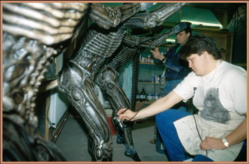 Deux maquettistes peignant à l'aérographe une grande figurine de l'Alien d'Alien 3 en atelier