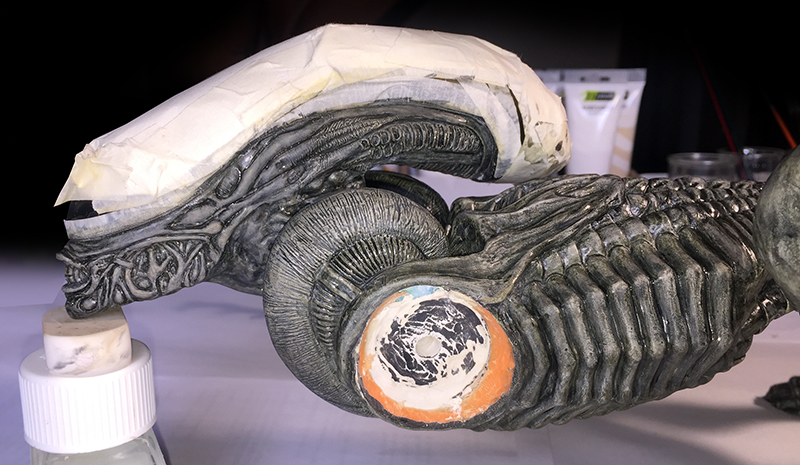 Tête de Xénomorphe Alien 3 en cours de peinture, crâne masqué de ruban adhésif sur l'établi
