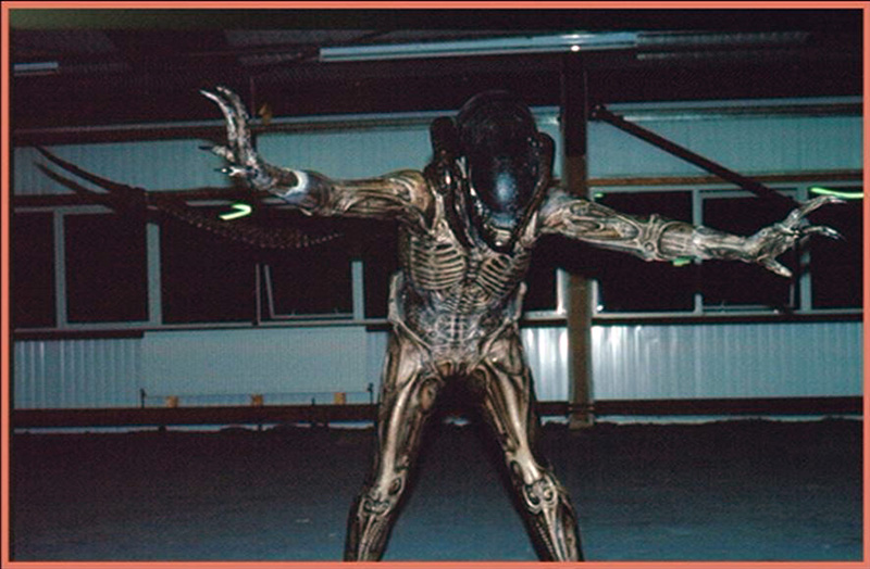 Costume grandeur nature du xénomorphe d'Alien 3 bras écartés dans un hangar sombre