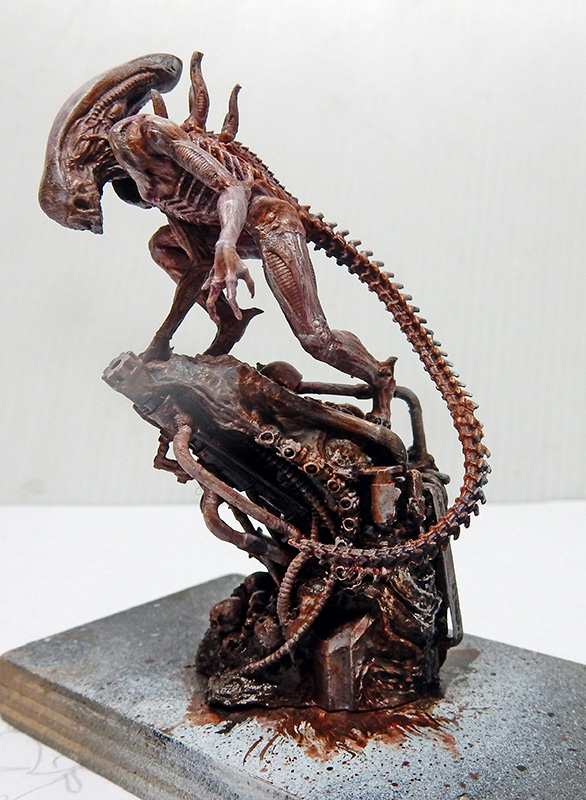 Maquette peinte d'un Alien xénomorphe brun perché sur un socle de tuyaux mécaniques