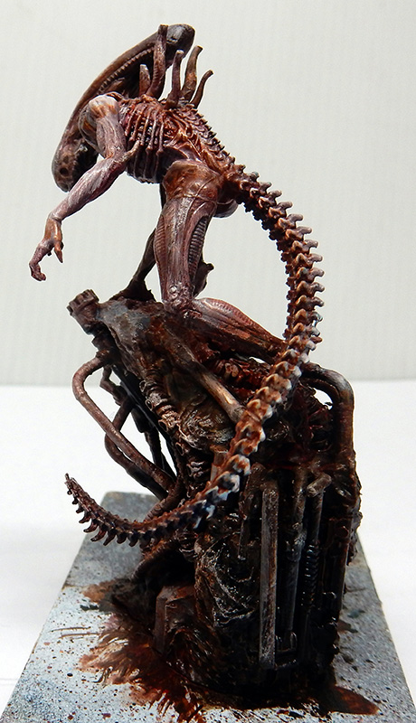 Maquette d'Alien xénomorphe brun-rouge dressé sur un socle mécanique avec sa longue queue enroulée