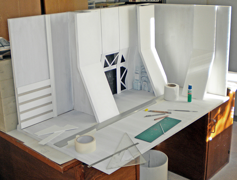 Construction en cours du décor blanc en carton plume sur l'établi, outils de découpe autour