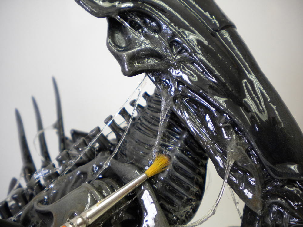 Gros plan sur la tête de la reine Alien recevant des filaments de bave au pinceau