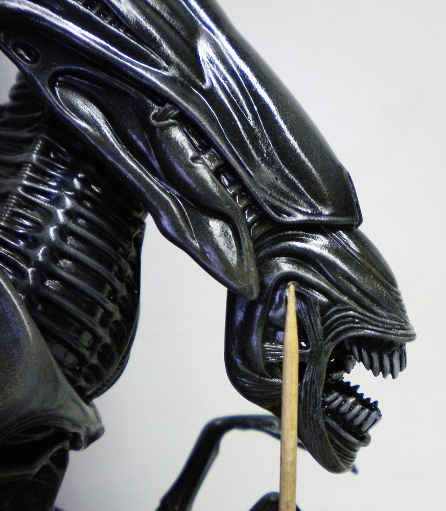 Gros plan sur la tête bleutée d'une maquette d'Alien aux mâchoires ouvertes lors de la peinture