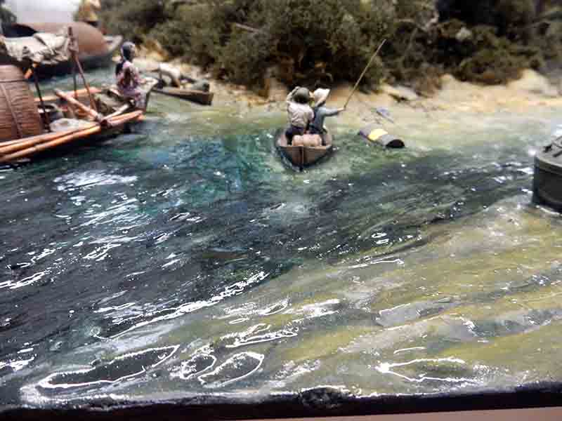 Diorama de rivière avec figurines en barque et radeau près d'une berge végétalisée