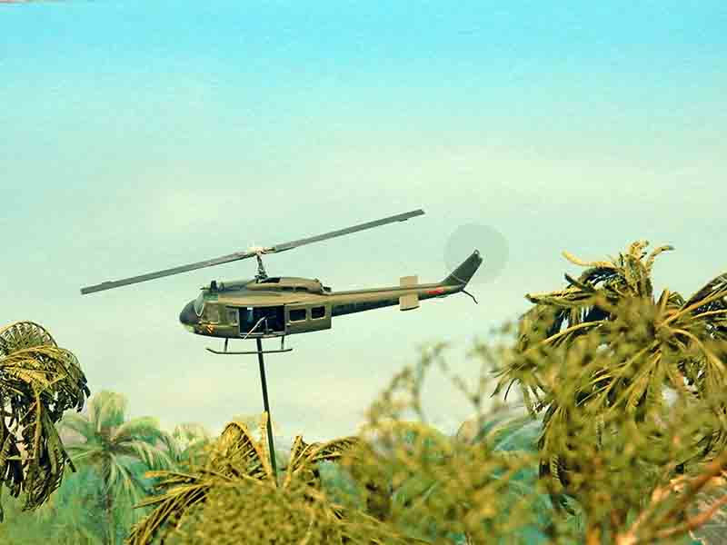 Maquette d'hélicoptère militaire UH-1 en vol au-dessus de palmiers dans un diorama tropical
