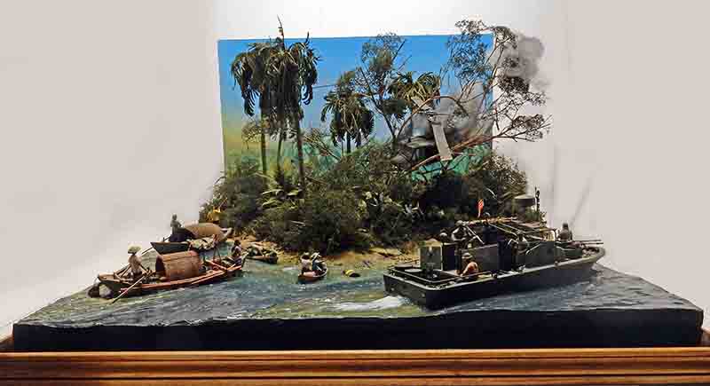 Diorama de jungle vietnamienne avec rivière, sampans, patrouilleur militaire et hélicoptère écrasé fumant
