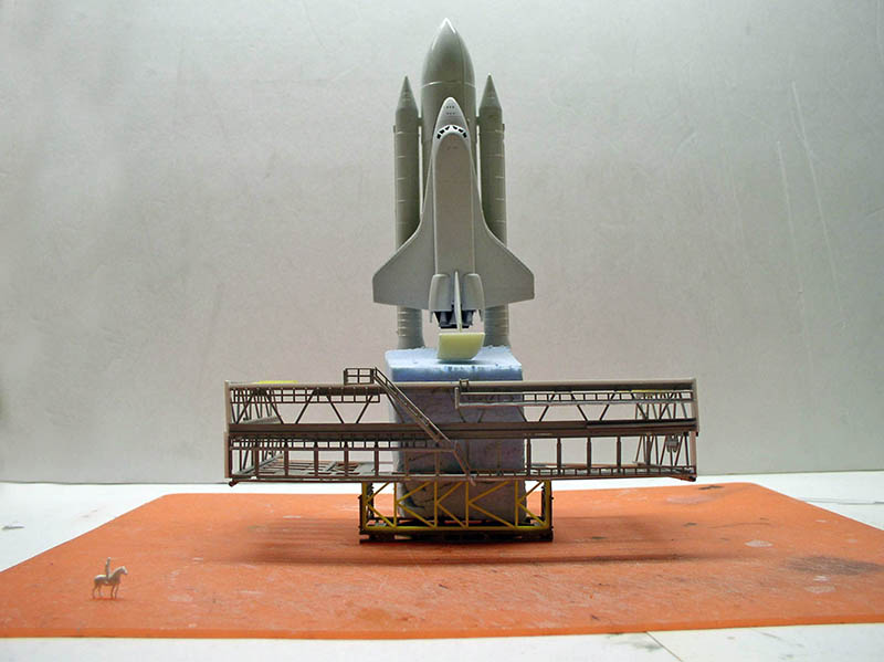 Maquette de navette spatiale gris clair dressée sur sa plateforme de lancement avec passerelles