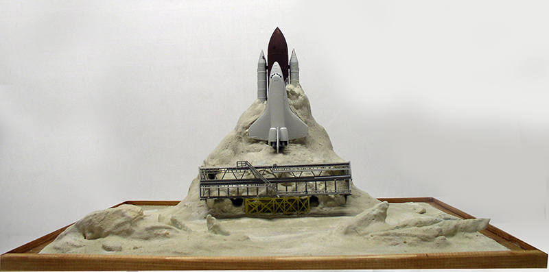 Maquette de navette spatiale avec boosters sur un diorama de terrain rocheux clair