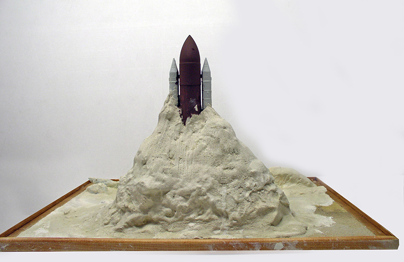 Maquette de fusée émergeant d'une montagne blanche sur un socle triangulaire en bois