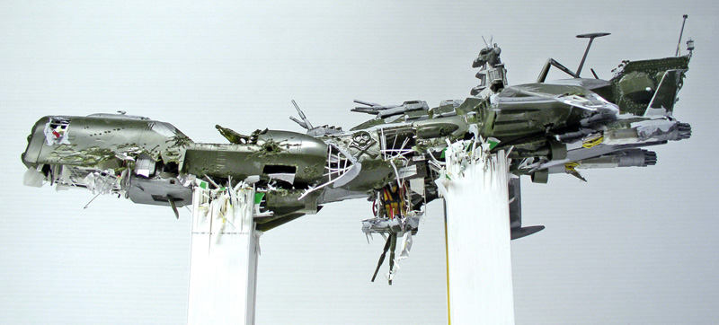 Maquette du vaisseau Arcadia d'Albator accidenté, coque verte éventrée et structures déchiquetées sur supports transparents