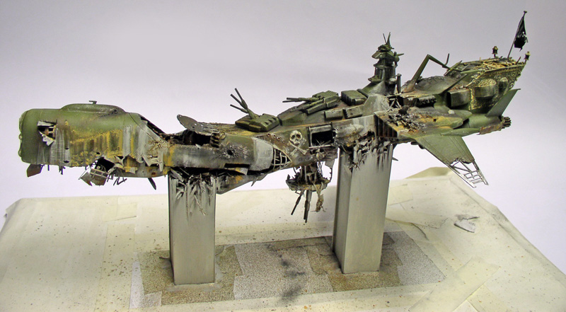 Maquette du vaisseau Arcadia d'Albator écrasé, coque verte endommagée posée sur supports métalliques
