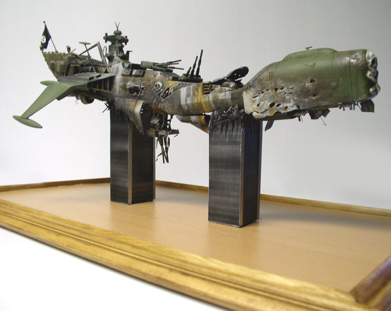 Maquette du vaisseau Arcadia d'Albator endommagé, posée sur deux supports métalliques et socle bois