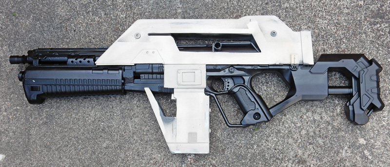 Réplique de fusil futuriste pour cosplay, corps blanc et noir, posée sur béton