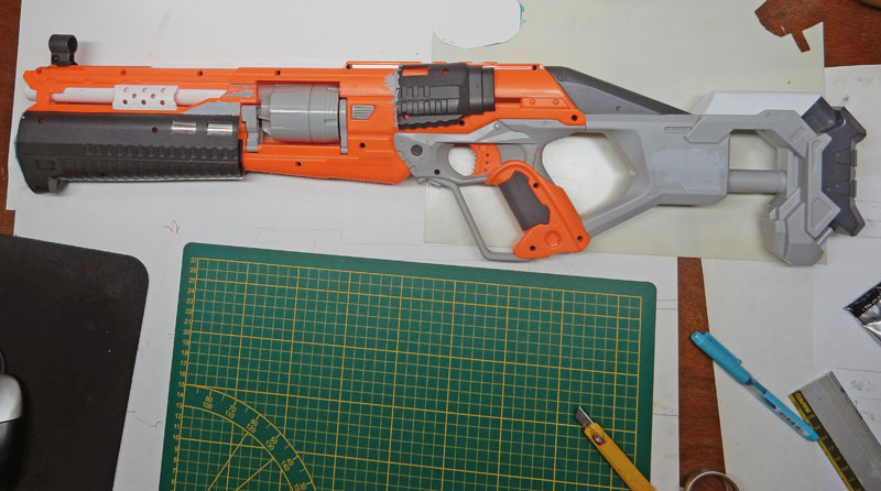 Pistolet Nerf orange et gris en cours de modification posé sur un tapis de découpe vert