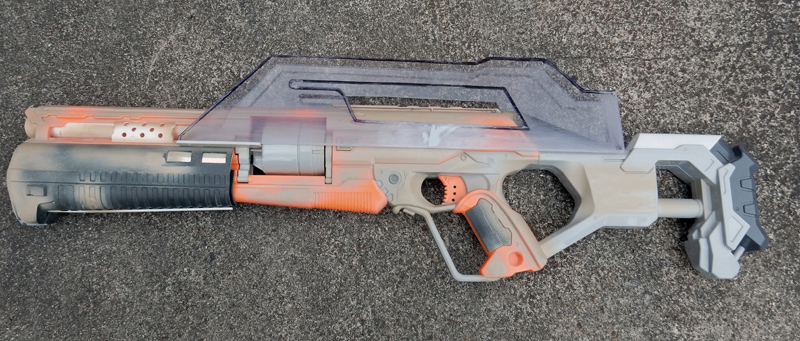 Fusil de cosplay futuriste peint en beige, orange et gris posé au sol
