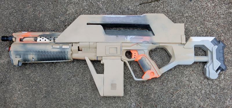 Réplique de fusil futuriste en carton peint pour cosplay posée sur le sol