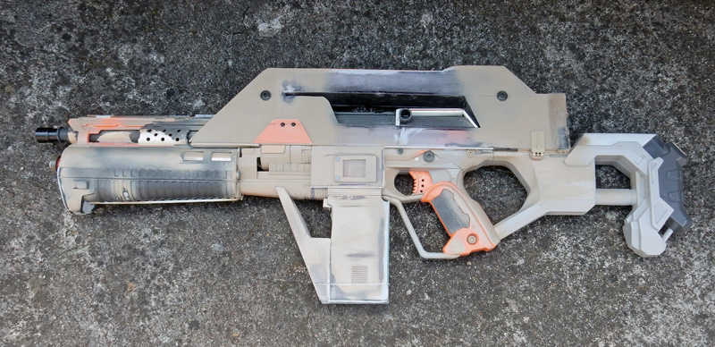 Réplique de fusil futuriste pour cosplay peinte effet usé posée sur béton