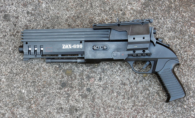 Pistolet de cosplay futuriste noir marqué ZOX-699 posé sur du béton